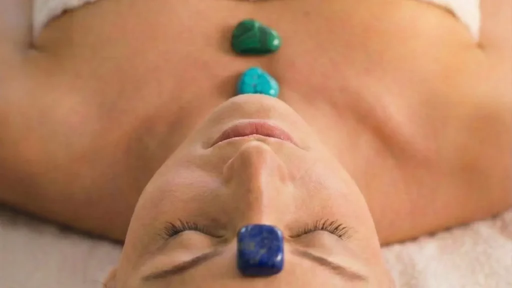 Visage détendu avec des pierres colorées posées sur les chakras, illustrant l'harmonie et la sérénité du massage énergétique.