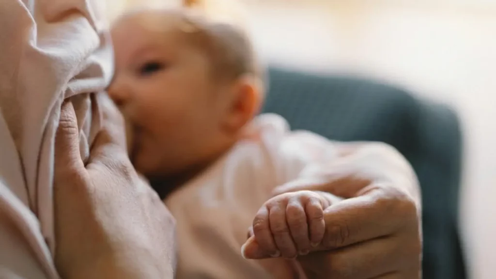 Gros plan d'un bébé allaité dont la petite main tient doucement le doigt de sa mère.
