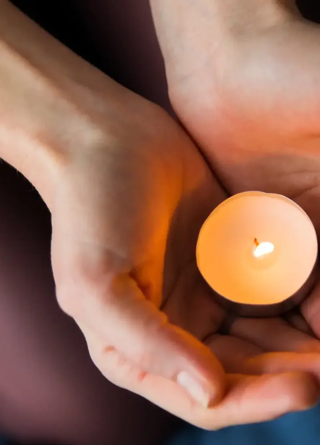 Mains tenant délicatement une bougie allumée, symbolisant la transmission de chaleur et l'apaisement du soin énergétique