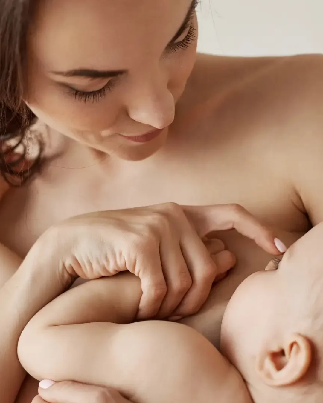 Mère souriante en contact peau à peau avec son bébé, le touchant doucement sur le nez, illustrant un moment de complicité après l'allaitement.