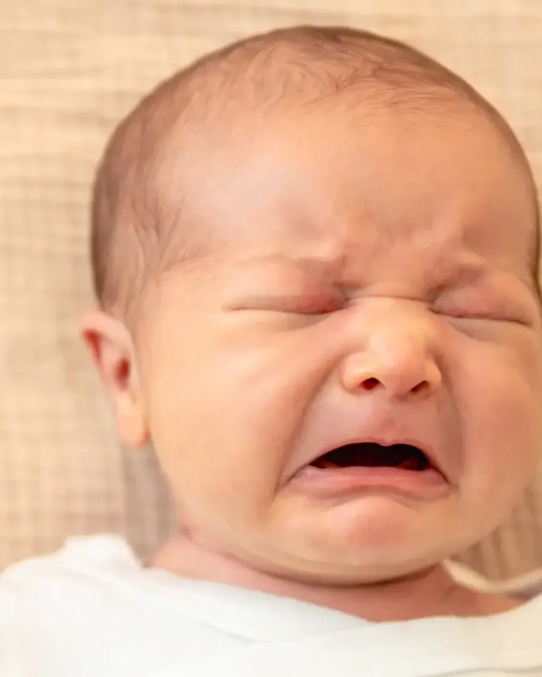 Gros plan sur le visage d'un nouveau-né qui pleure, les yeux fermés et la bouche ouverte, exprimant un besoin ou un inconfort, selon le langage silencieux des bébés