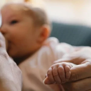 Gros plan d'un bébé allaité dont la petite main tient doucement le doigt de sa mère.
