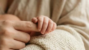 Gros plan d'une main de bébé agrippant le doigt d'un adulte sur une couverture en tricot, illustrant la communication non verbale.