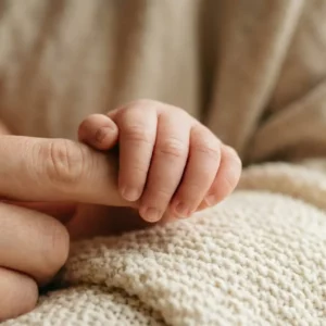 Gros plan d'une main de bébé agrippant le doigt d'un adulte sur une couverture en tricot, illustrant la communication non verbale.